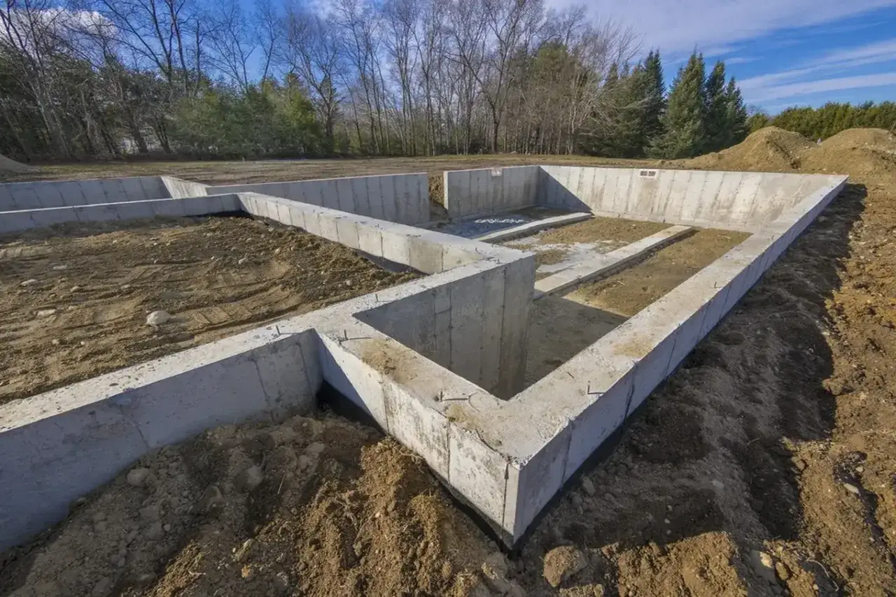 Beton na fundamenty w kształcie prostokąta, gotowy do budowy domu. Widać zbrojenie i ziemię wokół.
