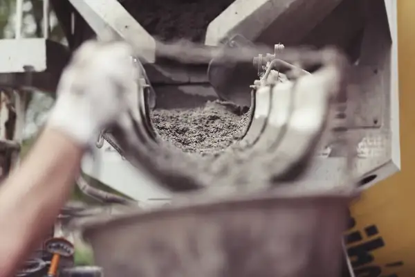 Ręka w białej rękawiczce wsypuje cement do maszyny.